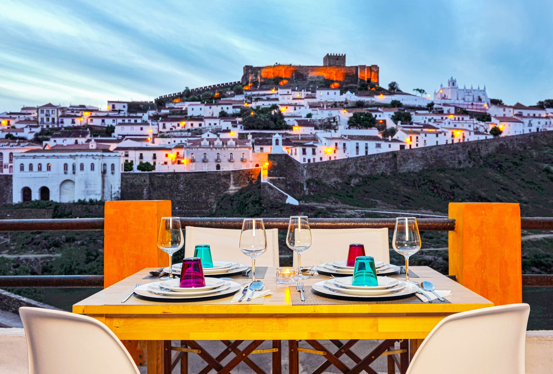 Mesa posta na esplanada da Casa Amarela ao anoitecer, com vista para o castelo iluminado de Mértola